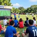 Excited fans enjoying live football matches on LuongSonTV in a community park.